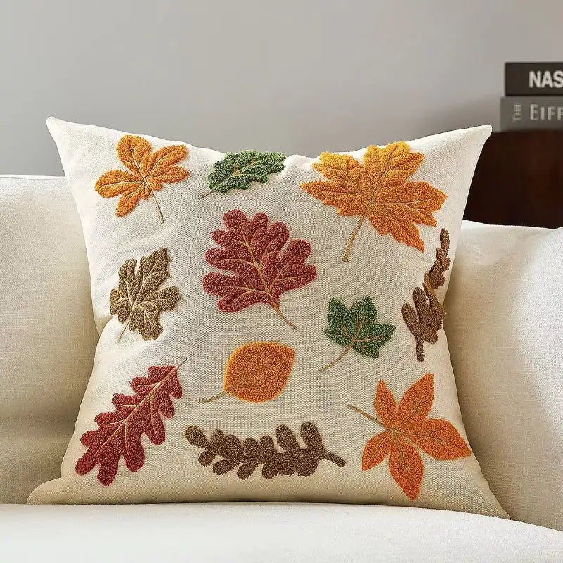 Decorative pillow with embroidered autumn leaves on a beige couch.