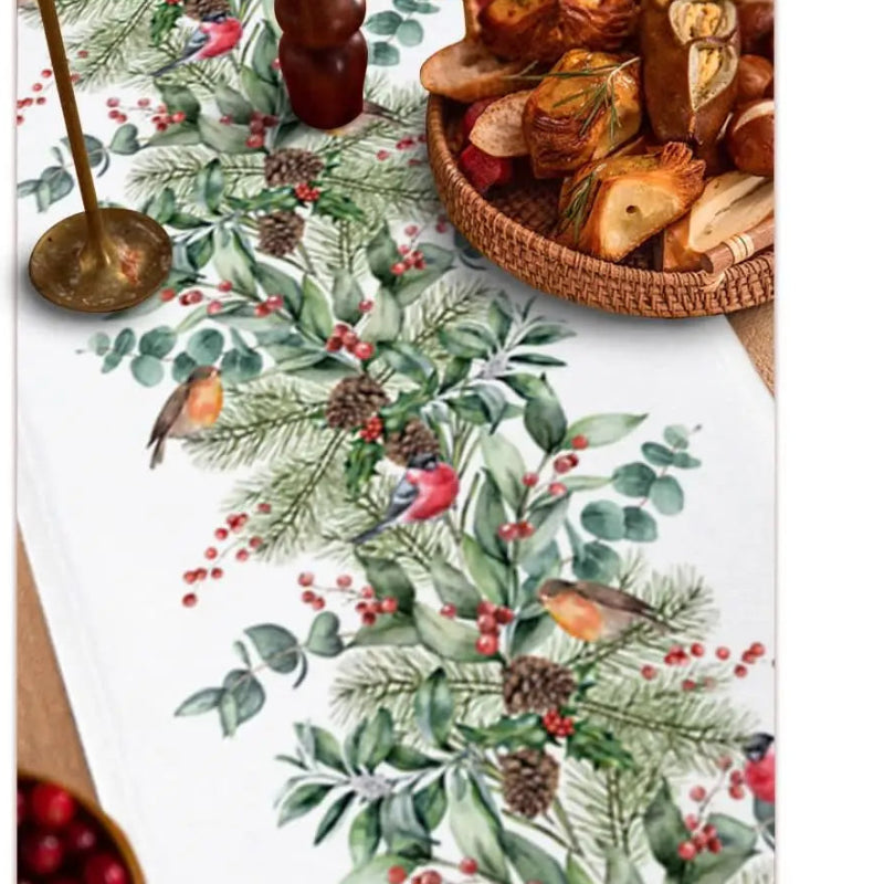 Christmas garland banner with a festive green pine and eucalyptus pattern, red berries, pinecones, and small birds, shown laid out on a table alongside a size measurement chart and a basket of bread.