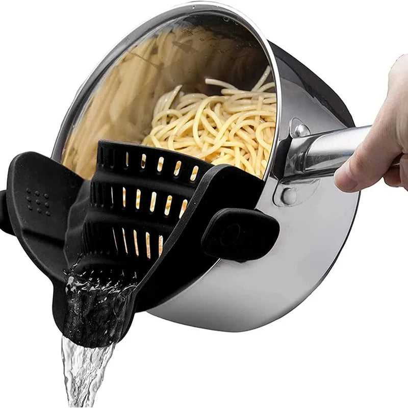 Pasta being drained from a pot using a black pasta strainer.