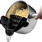 Pasta being drained from a pot using a black pasta strainer.