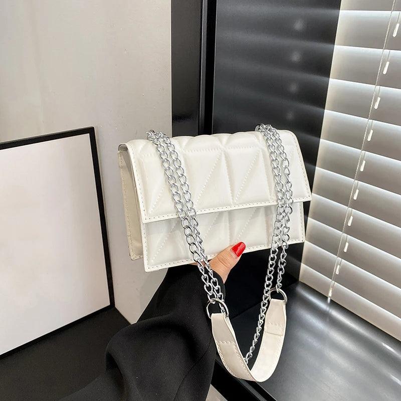 White handbag with a chain strap held by a hand against a neutral background