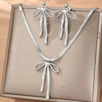 Silver bow-shaped necklace and earrings on a beige background