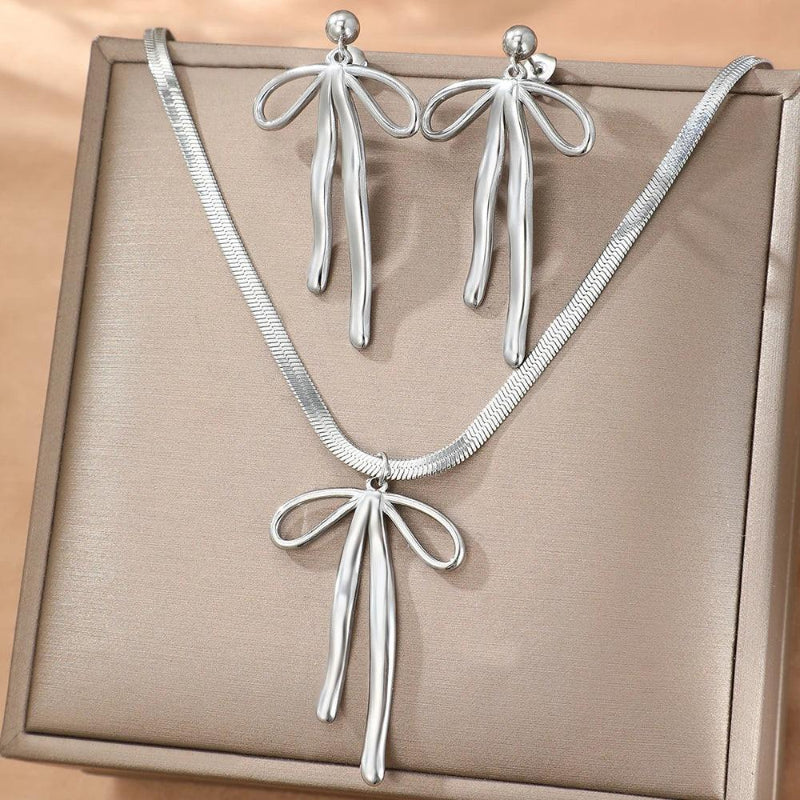 Silver bow-shaped necklace and earrings on a beige background