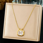 Gold necklace with a clear pendant on a beige box
