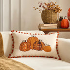 Decorative pillow with pumpkins on a couch, with a cozy autumn setting.