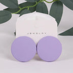 Purple round earrings on a white jewelry box with green leaves in the background