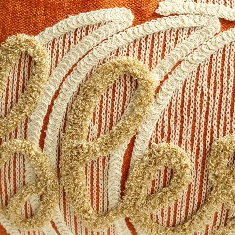 Close-up of a woven textile with a rust orange and cream striped background and large raised beige embroidered script lettering.