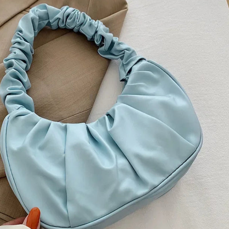 Light blue satin hair bonnet held by a hand with beige coat and white pants in the background