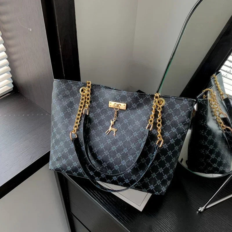 Designer handbag with gold chains and a keychain on a reflective surface.