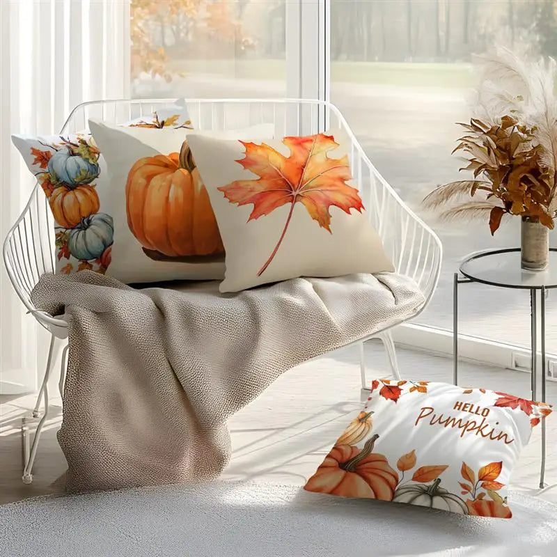 Three decorative throw pillows with autumn and pumpkin illustrations are styled on a white wire chair draped with a beige knit blanket in a bright room. One pillow at the bottom right reads 'Hello Pumpkin'.