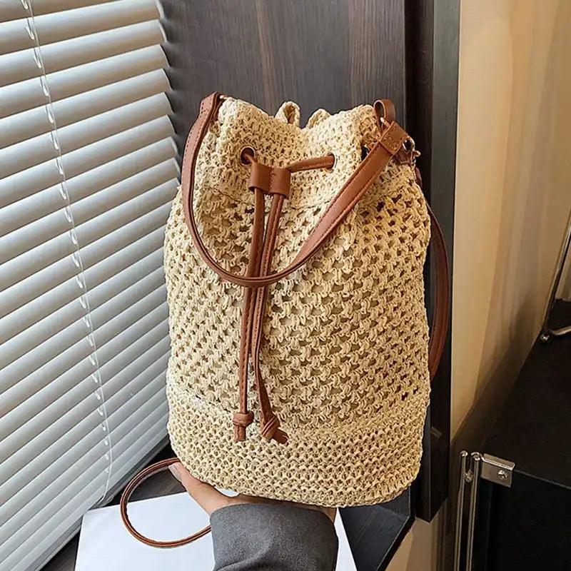 Beige woven drawstring bag with brown leather straps held by a person indoors.