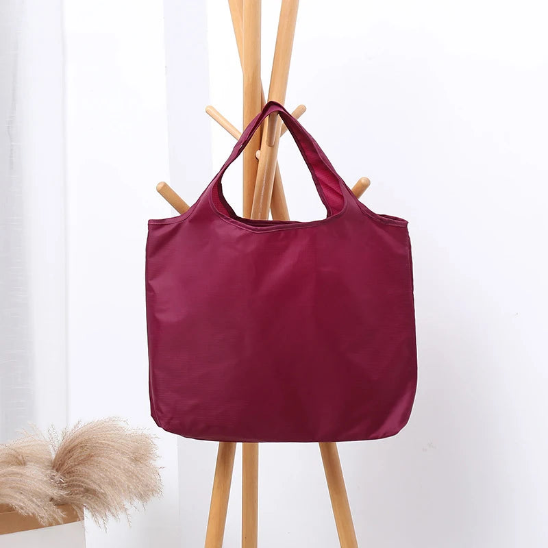 Maroon tote bag hanging on a wooden coat rack against a white background