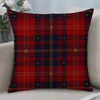 A square throw pillow with a red and navy blue tartan plaid pattern featuring small gold star details, resting on a light beige sofa next to a vase of white roses.