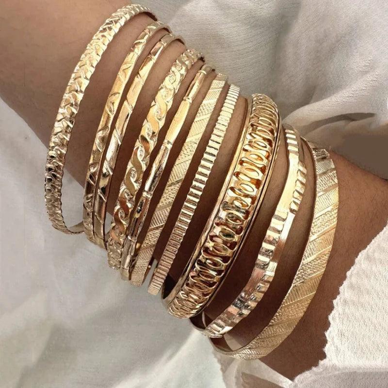 Gold bracelets on a wrist against a neutral background