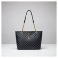 Black patterned handbag with gold chain and handle against a white wall.