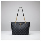 Black patterned handbag with gold chain and handle against a white wall.