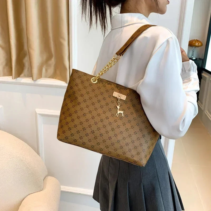 Person holding a brown patterned handbag with a gold chain strap indoors.