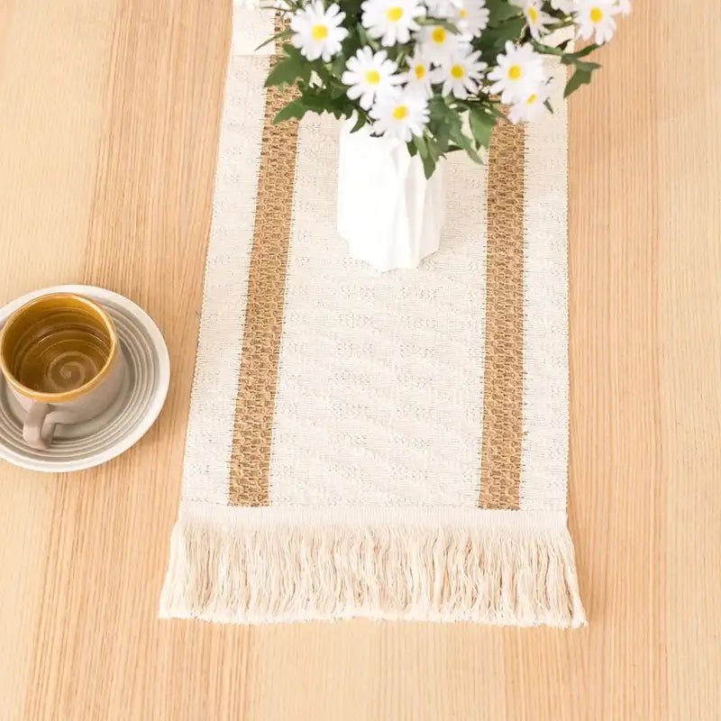 Beige and white striped table runner with a vase of daisies on a wooden surface.