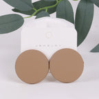 Brown round earrings on a white jewelry card with green leaves in the background