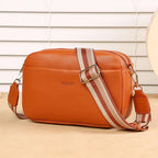 Orange leather bag with a striped strap on a beige surface
