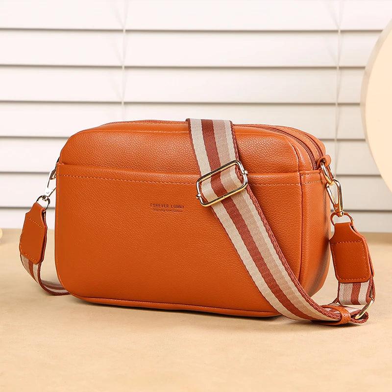 Orange leather bag with a striped strap on a beige surface
