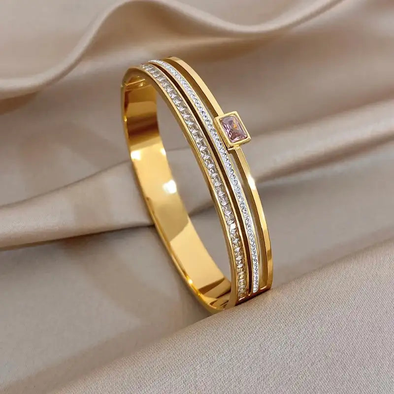Gold bracelet with a pink gemstone on a beige fabric background
