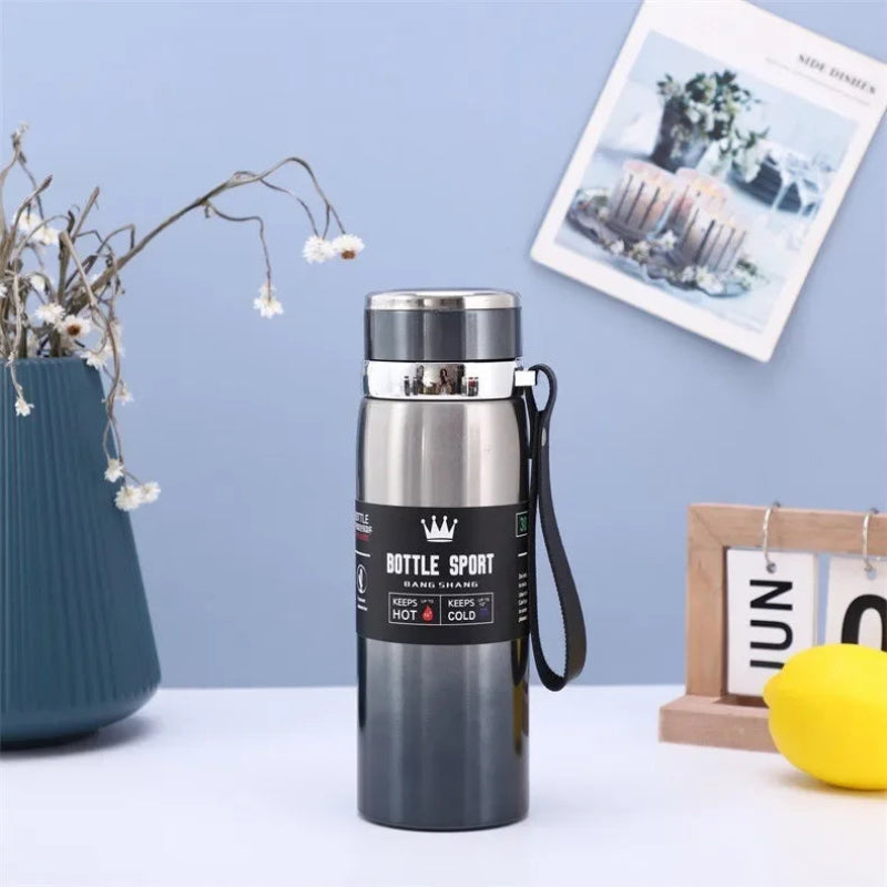Black insulated bottle with silver lid on a white surface against a light blue wall.
