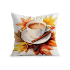 A square white throw pillow featuring a printed autumn-themed design of a white coffee cup on a saucer with a cinnamon stick, surrounded by orange, yellow, and red maple leaves.