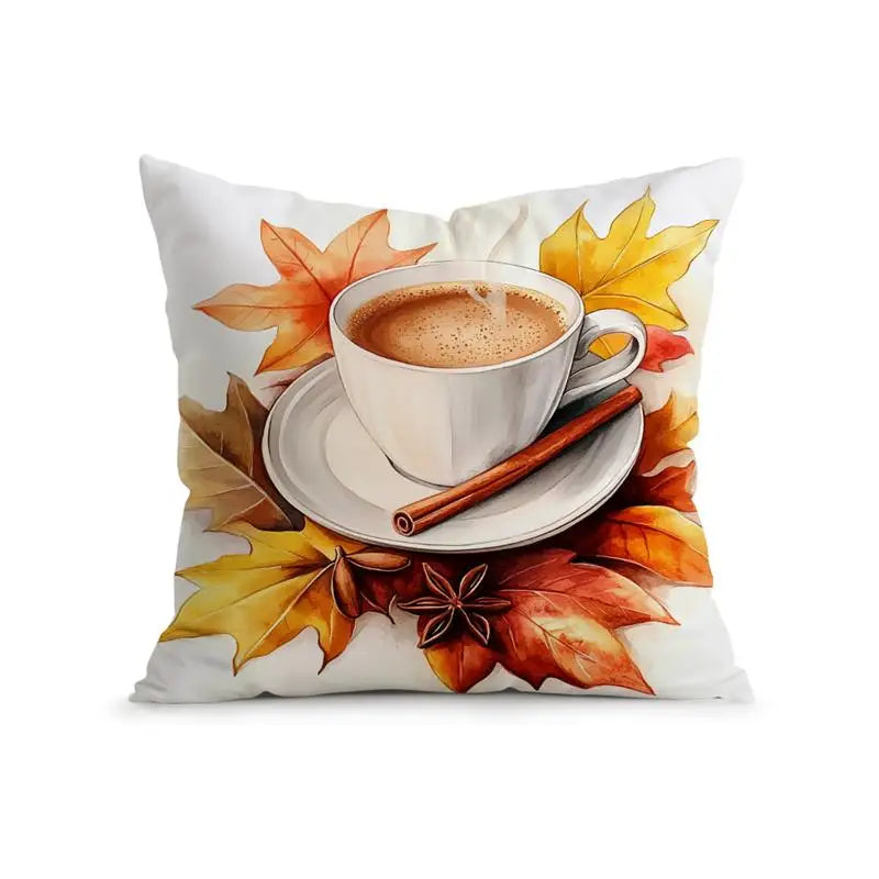 A square white throw pillow featuring a printed autumn-themed design of a white coffee cup on a saucer with a cinnamon stick, surrounded by orange, yellow, and red maple leaves.