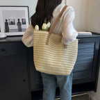 Person holding a woven bag with tulips, standing in a room with a black cabinet and framed pictures.