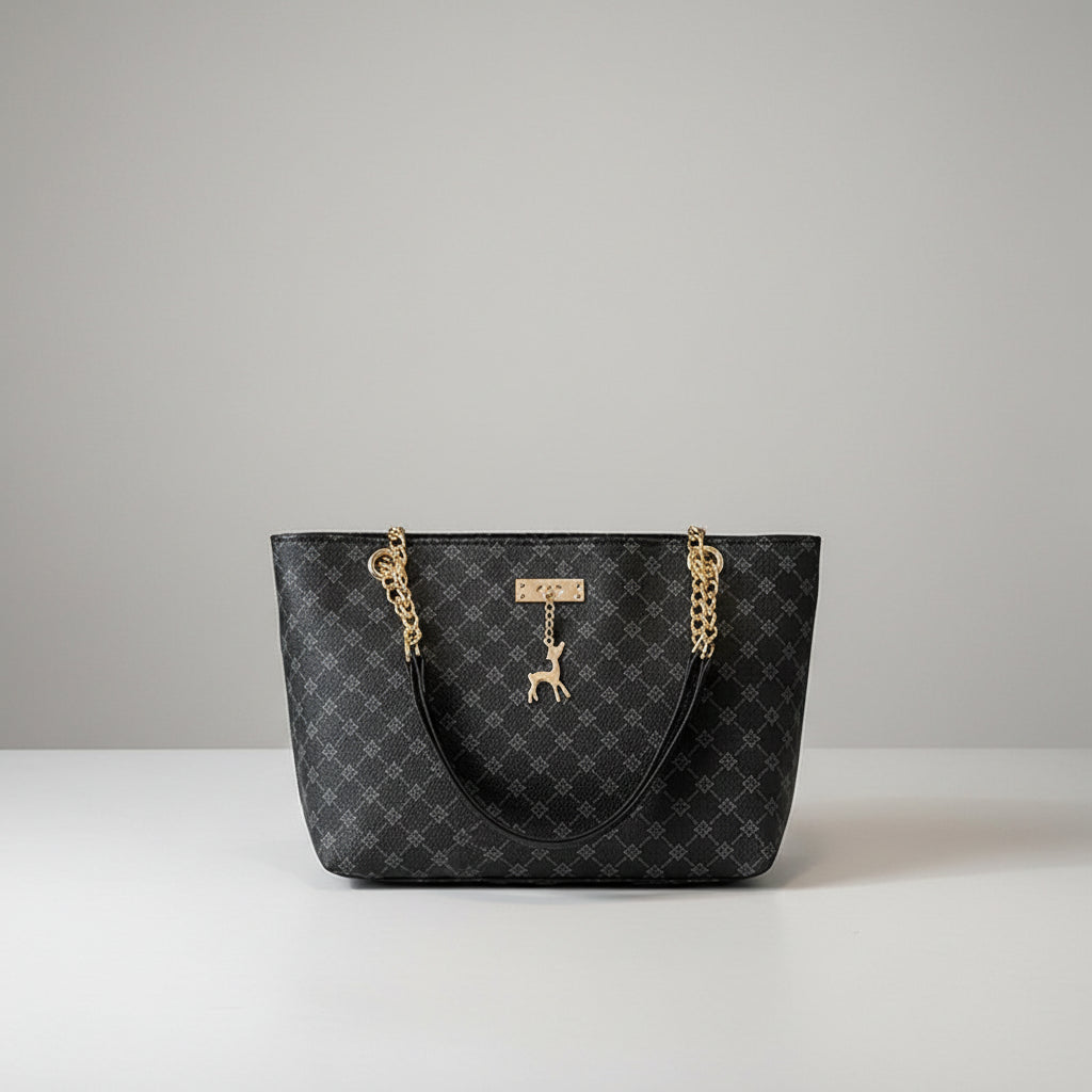 Black patterned handbag with gold chains and a deer charm on a wooden surface.