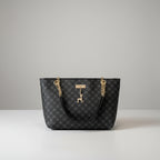 Black patterned handbag with gold chains and a deer charm on a wooden surface.