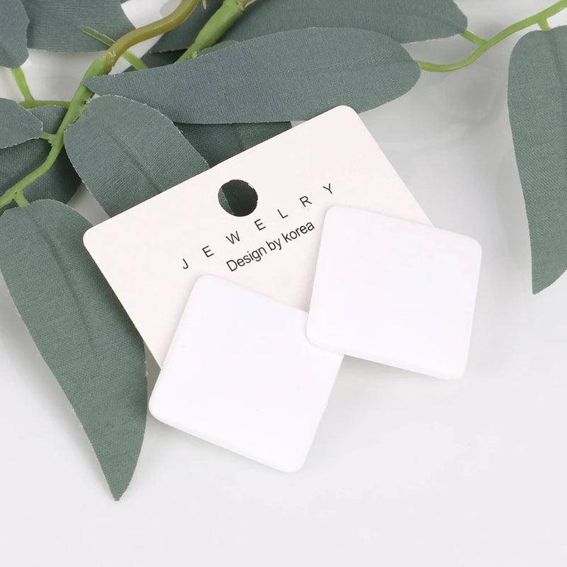 White square earrings on a jewelry card with green leaves in the background