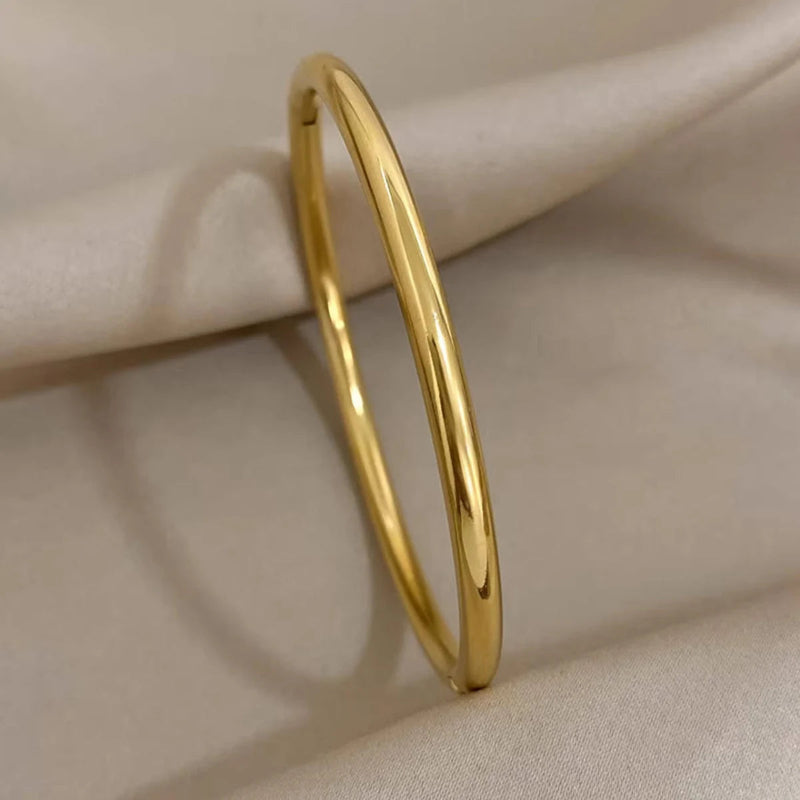 A polished yellow gold bangle bracelet resting on draped cream-colored fabric.