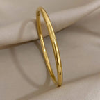 A polished yellow gold bangle bracelet resting on draped cream-colored fabric.