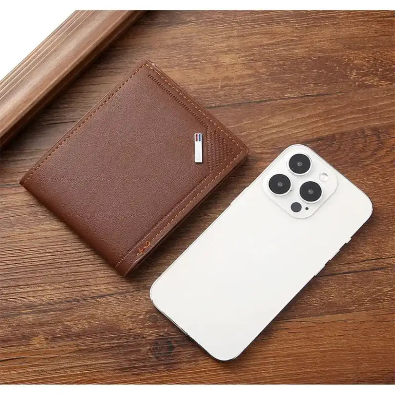 Brown leather wallet and white phone on a wooden surface