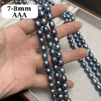 A hand holds three strands of dark gray to black iridescent baroque pearls, with a white text label reading '7-8mm AAA' in the top left. More strands of pearls are draped over a light beige jewelry box in the background.
