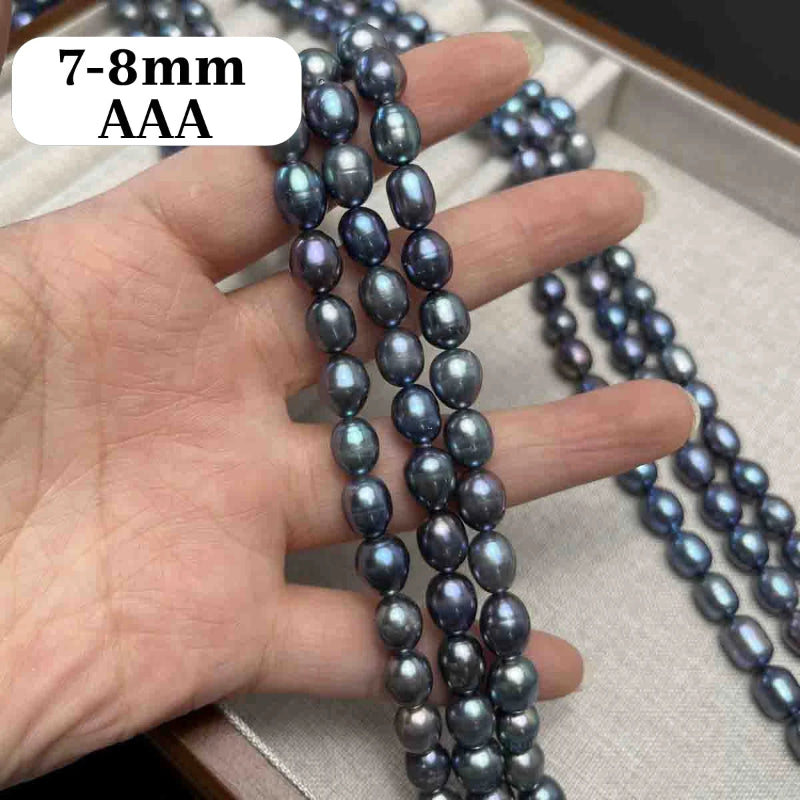 A hand holds three strands of dark gray to black iridescent baroque pearls, with a white text label reading '7-8mm AAA' in the top left. More strands of pearls are draped over a light beige jewelry box in the background.