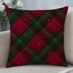A square throw pillow with a red and green Christmas plaid pattern and small gold star accents, resting on a light beige sofa next to a vase of white roses.
