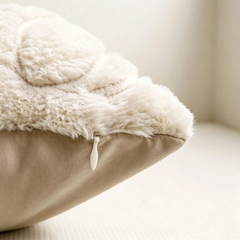 Close-up of a plush cream sherpa or faux-fur cushion cover layered over a beige pillow, with a small white pull tab visible at the edge, set against a soft neutral indoor background.