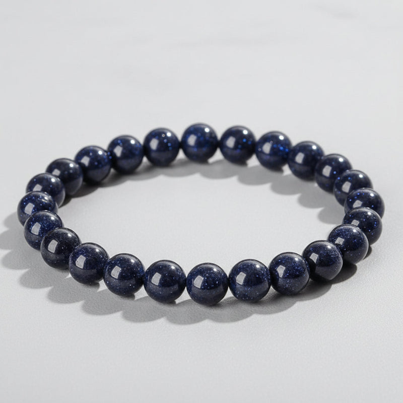 A beaded stretch bracelet made of glossy dark blue gemstone beads with tiny gold speckles, displayed on a wood slice. The text 'Self-Love' and 'Promote self-acceptance' is overlaid on the image.