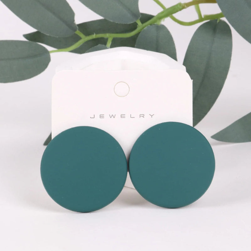 Teal round earrings on a white jewelry card with green leaves in the background