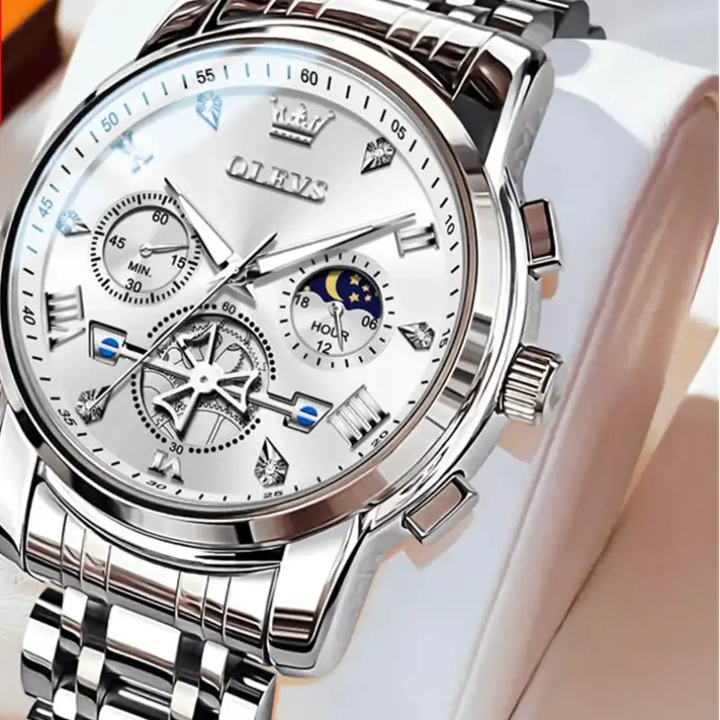 Silver wristwatch with detailed face on a white cushion, brand 'OLEVS' visible