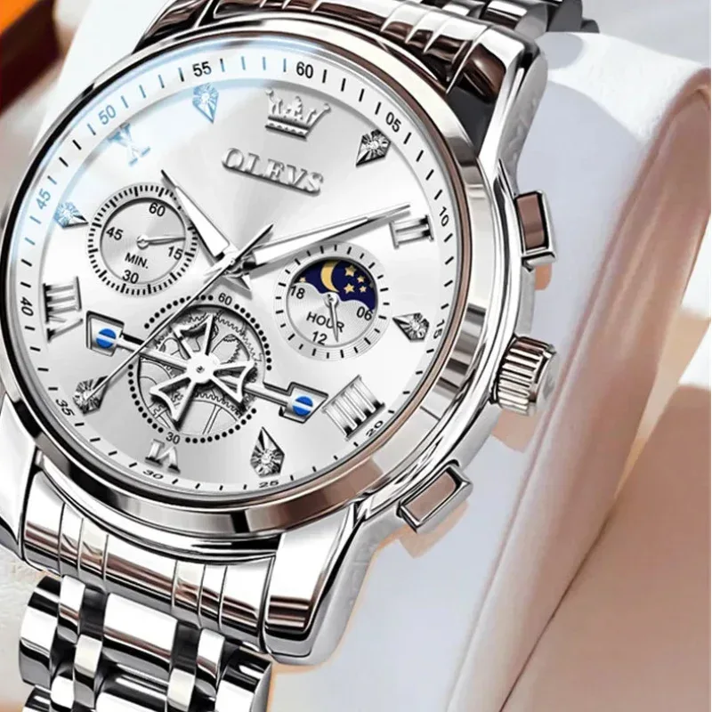 Silver wristwatch with detailed face on a white cushion, brand 'OLEVS' visible