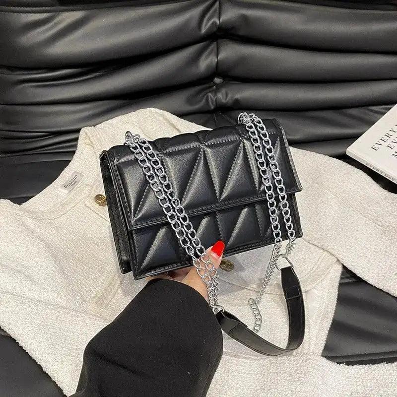 Black quilted handbag with chain strap held by a person against a black leather couch.