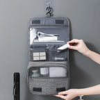 Gray hanging toiletry bag with compartments filled with travel items on a gray background