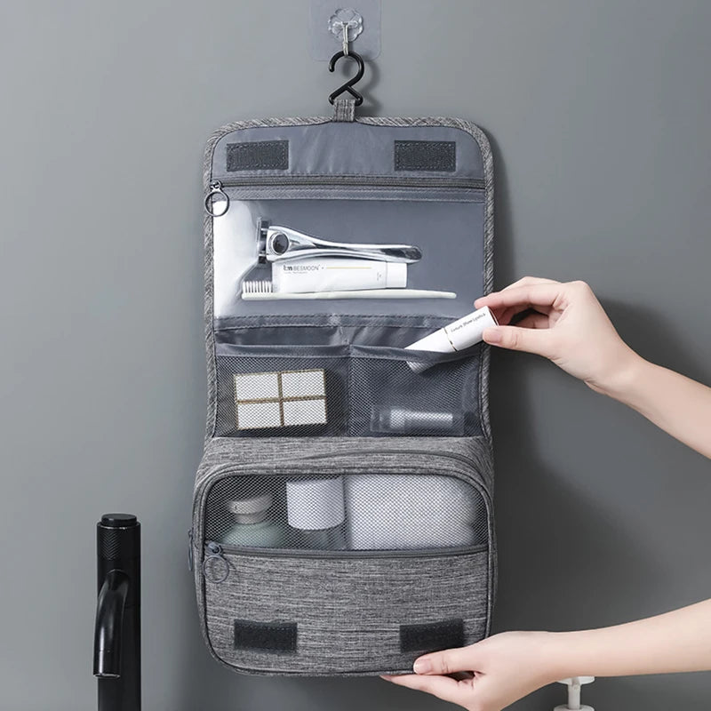 Gray hanging toiletry bag with compartments filled with travel items on a gray background