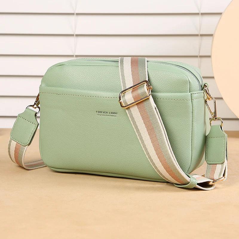 Green handbag with a striped strap on a beige surface