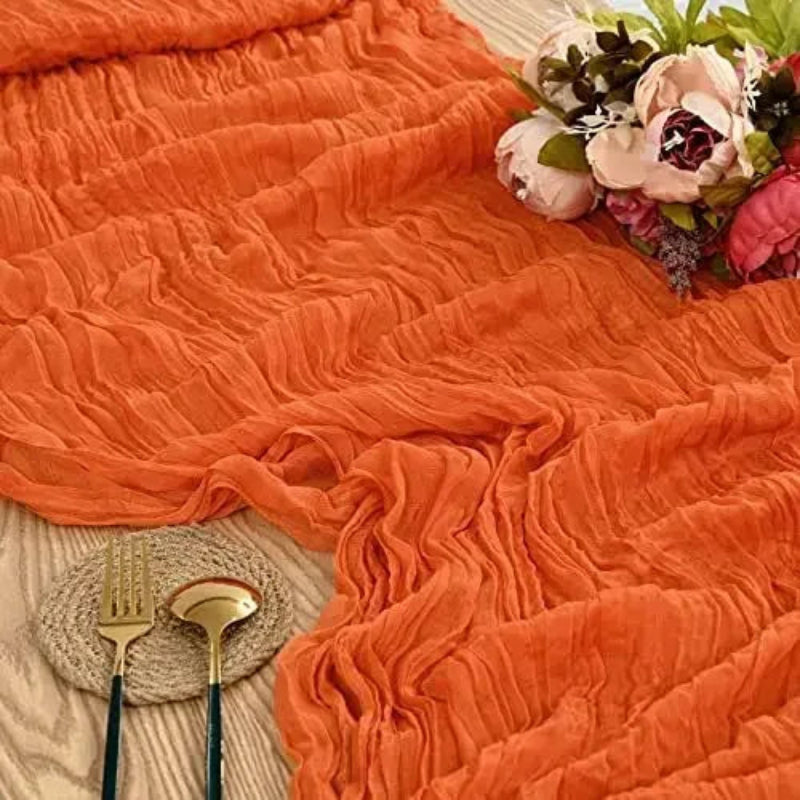 Orange textured blanket with floral arrangement and cutlery on a textured surface