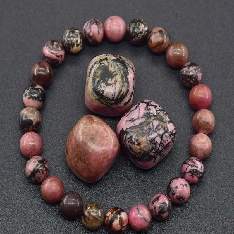A beaded bracelet made of polished pink and black marbled tumbled stones, arranged in a circle with three larger matching tumbled stones on a dark gray textured background.